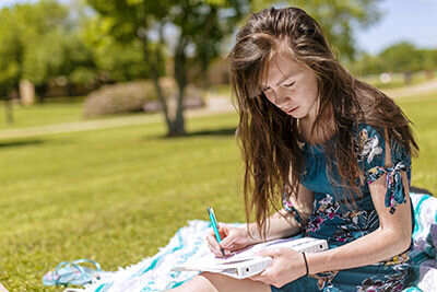 Girl, sitting in grass, writing
